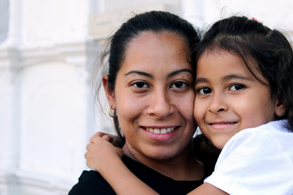 A woman of colour with her daughter smile at the camera