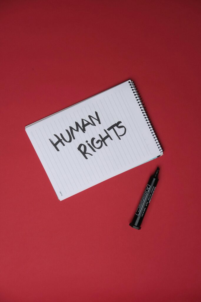 A white notepad with handwritten text that says 'human rights', next to a black marker on a dark red background.